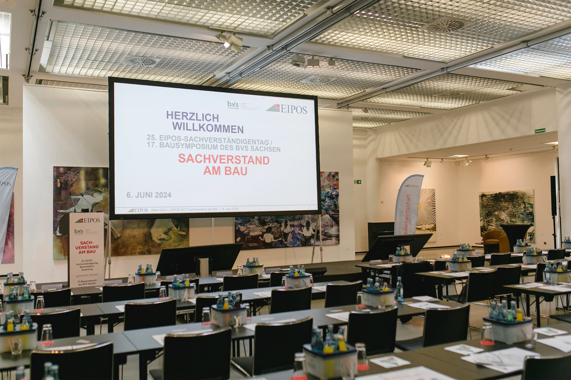 Heller Konferenzraum mit Möbelierung und der Eröffnungspräsentation des EIPOS Sachverständigentages "Sachverstand am Bau"